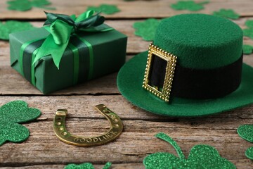 St. Patrick's day. Leprechaun hat, golden horseshoe, green gift box and decorative clover leaves on wooden background - obrazy, fototapety, plakaty