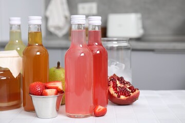 Tasty kombucha in glass bottles, jar and fresh fruits on white tiled table