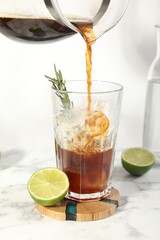 Pouring coffee into glass with ice cubes at white marble table
