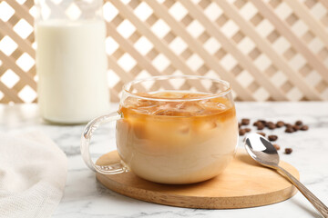 Refreshing iced coffee with milk in glass cup and spoon on white table