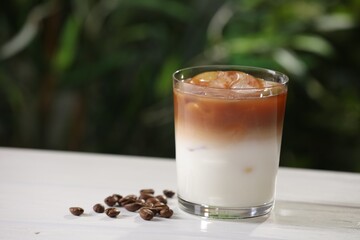 Glass of iced coffee and beans on white wooden table outdoors. Space for text