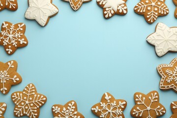 Fototapeta na wymiar Frame made of tasty star shaped Christmas cookies with icing on light blue background, flat lay. Space for text