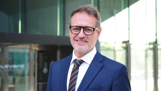 Individual footage of a handsome corporate business man smiling and looking at camera wearing a formal blue suit at workplace. Real successful executive male or ceo staring front. 50s businessperson