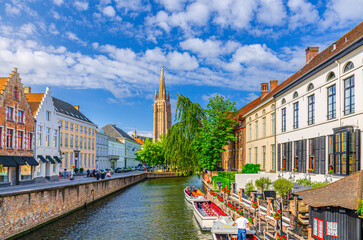 Naklejka premium Bruges cityscape, Roman Catholic Church of Our Lady, Dijver water canal with promenade embankment, boat near wharf and medieval buildings, Brugge old town, Bruges city centre, Flemish Region, Belgium