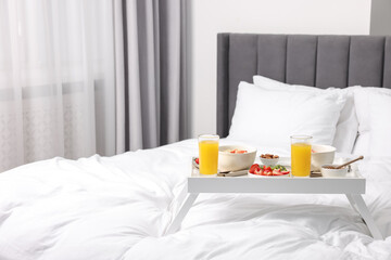 Tasty breakfast served in bed. Oatmeal, juice, fruits, almonds and honey on tray, space for text