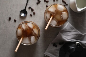 Refreshing iced coffee with milk in glasses, ingredients and spoon on gray table, flat lay