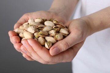 Woman holding handful of tasty pistachios on grey background, closeup