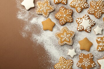 Tasty Christmas cookies with icing and powdered sugar on brown background, flat lay. Space for text