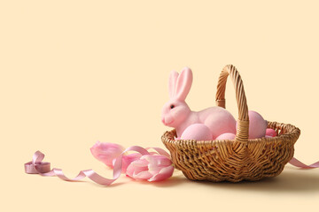 Wicker basket with painted Easter eggs, toy bunny and tulip flowers on yellow background