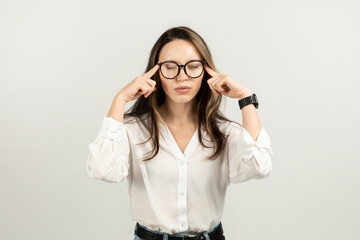 Focused young woman with brown hair wearing glasses and a white blouse holds temples