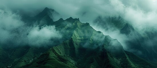 Clouds engulfing the peaks of a towering green mountain, creating a misty and mysterious atmosphere.