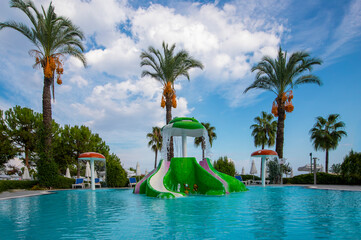 A cloudy sky, date trees, a clean pool and water slides.​