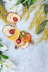 Homemade fruit chips on a light background. Dried slices of apple, pear, orange, persimmon and kiwi. A healthy snack. Organic fruits. Branches of flowering mimosa. Flat lay. Top view. Copy space.