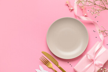 Festive Easter table setting decorated with gifts and eggs on pink background