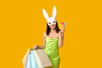 Beautiful young woman in bunny ears with shopping bags and credit cards on yellow background....