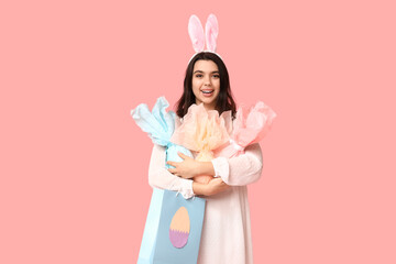 Beautiful young happy woman in bunny ears with shopping bag and Easter gift eggs on pink background