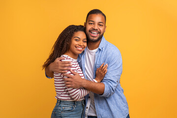 Loving black couple in warm embrace posing against yellow background
