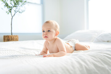 Adorable baby boy in white sunny bedroom.