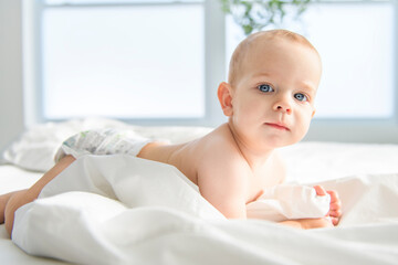 Adorable baby boy in white sunny bedroom.