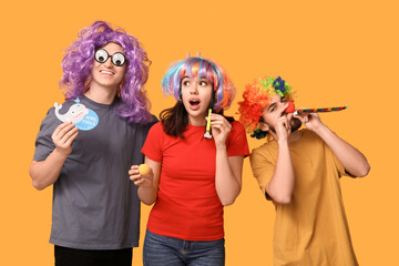 Young friends in funny disguise with whistles on yellow background. April fool's day celebration