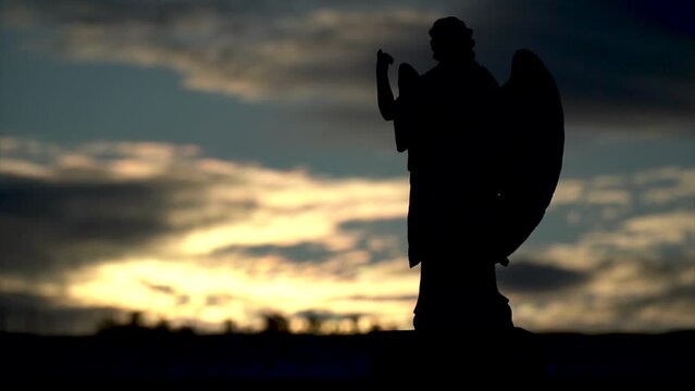 Slow motion, statue of an angel in the cemetery, backlit at sunset