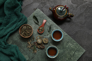 Ceramic plate with teapot and cups of aromatic puer tea on black background