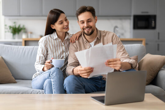 Smiling european couple with coffee and documents near laptop
