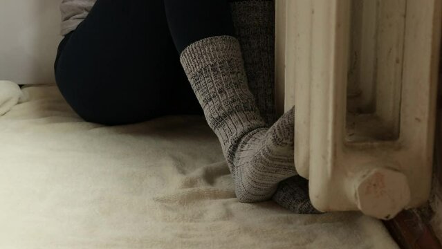Feet in socks on a cast iron radiator in an apartment, no heating, no heat in winter