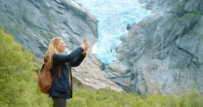 Woman, glacier and smartphone for pictures, travel and norway with backpack and sightseeing. Technology, adventure and nature for vacation, exploring and mountain in outdoor for winter holiday
