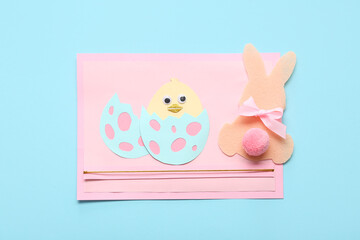 Paper Easter bunny and card with chicken on blue background. Top view