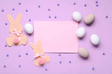 Easter eggs, felt bunnies and blank greeting card on lilac background