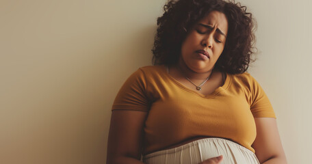 Worried young black woman, uncomfortable with painful cramps, overweight and pregnant, brown background