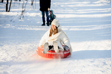 A young girl is tubing in a winter snowy forest with beautiful sunlight - obrazy, fototapety, plakaty