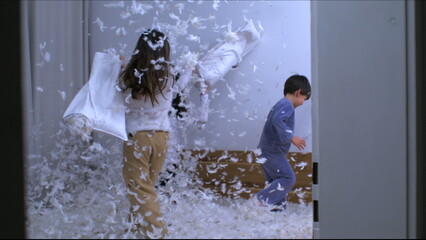 Happy moment of children and mom having a pillow fight with feathers flying everywhere in the air in slow motion 1000 fps, siblings standing in bed engaged in play