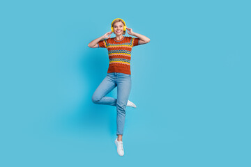 Fototapeta na wymiar Full size photo of positive cheerful woman dressed knit t-shirt denim trousers flying in headphones isolated on blue color background