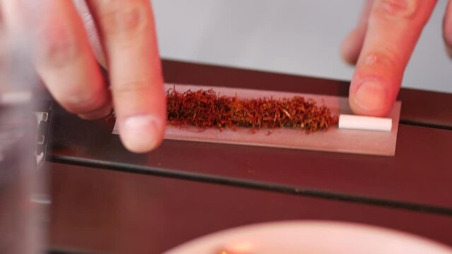 Man fingers rolls cigarette. Man prepares tobacco and tissue paper for rolling cigarette with hands. Smoking tobacco. Do it yourself cigarette. DIY smoking appliance. Pula, Croatia - February 3, 2024