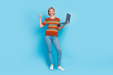 Full size photo of optimistic cheerful woman dressed knit t-shirt hold laptop showing v-sign symbol isolated on blue color background