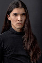 Fototapeta premium Handsome calm man. Trendy young man dressed in black shirt posing in modern studio against dark wall. Portrait of young guy with long straight hair. people, fashion, beauty concept