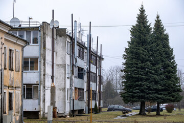 old damaged multiapartment building in Latvia countryside. Aged walls and window frames, metal chimneys, satellite dishes, soviet leftovers. Shelter for poor people