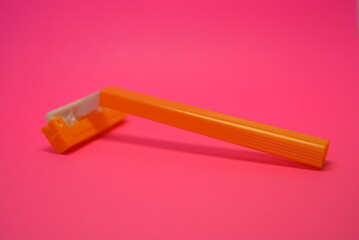 Things, personal care products, disposable, plastic, orange razor, located on pink background.