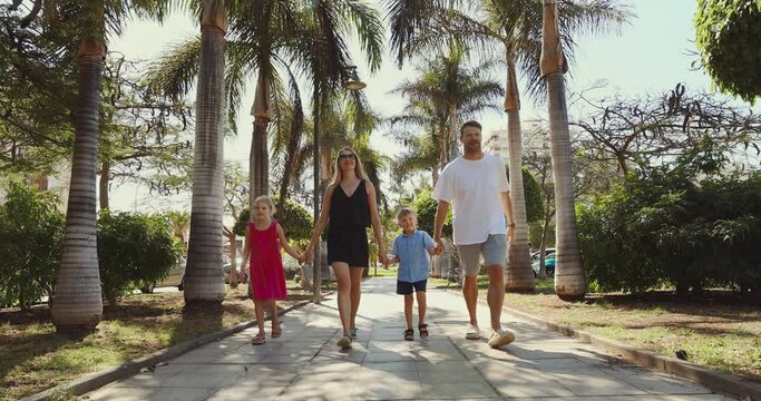 happy family with children walking in hands down an alley in a palm tree park in Tenerife, Spain. summer vacation