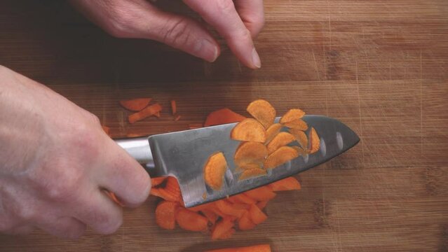 Top View male Chef Knife Cut Vegetables. Preparing vegetable salad. Man chopping carrot with knife on wooden cutting board. Slice carrots for healthy vegan recipe. Close-up slow motion knife cutting