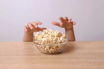 Children's hands are visible from under the table, trying to take popcorn from the table.