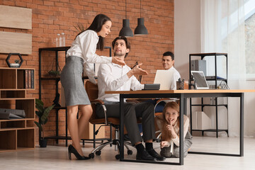 Fototapeta premium Young woman tying her colleague's shoe laces in office. April Fools' Day celebration