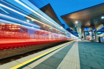 High speed train in motion at the railway station at night. Moving red modern intercity passenger...