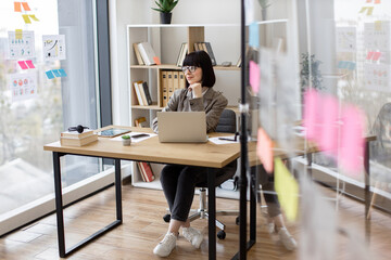 Confident caucasian woman in formal wear and glasses sitting with laptop at desk at modern company boardroom. Concept of modern technology and busy people.