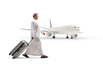Full length profile shot of a man in ethnic clothes pulling a suitcase and walking in front of an airplane