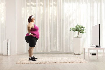 Full length profile shot of a plus size woman in sportswear standing in front of a tv