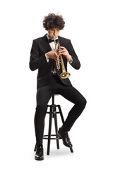 Naklejka premium Elegant young man in a black suit playing a trumpet and sitting on a chair