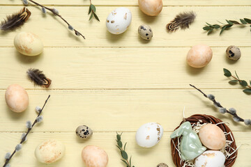 Painted Easter eggs with leaves, pussy willow branches and feathers on yellow wooden background